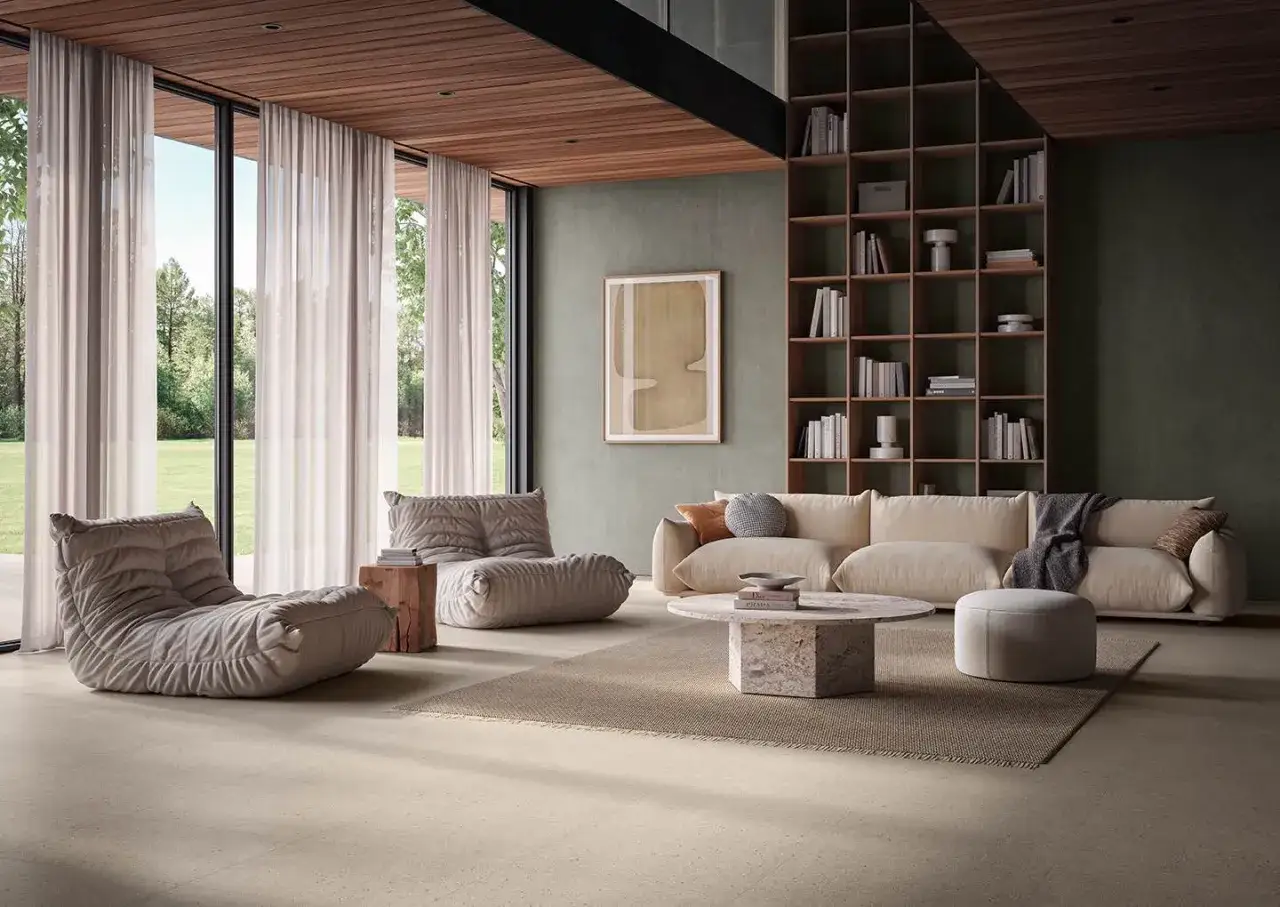 Sala de estar moderna con sof&aacute;s, mesa de centro de m&aacute;rmol y estanter&iacute;a. El suelo de tonos claros, con texturas que recuerdan a distintos tipos de suelo, complementa la decoraci&oacute;n.