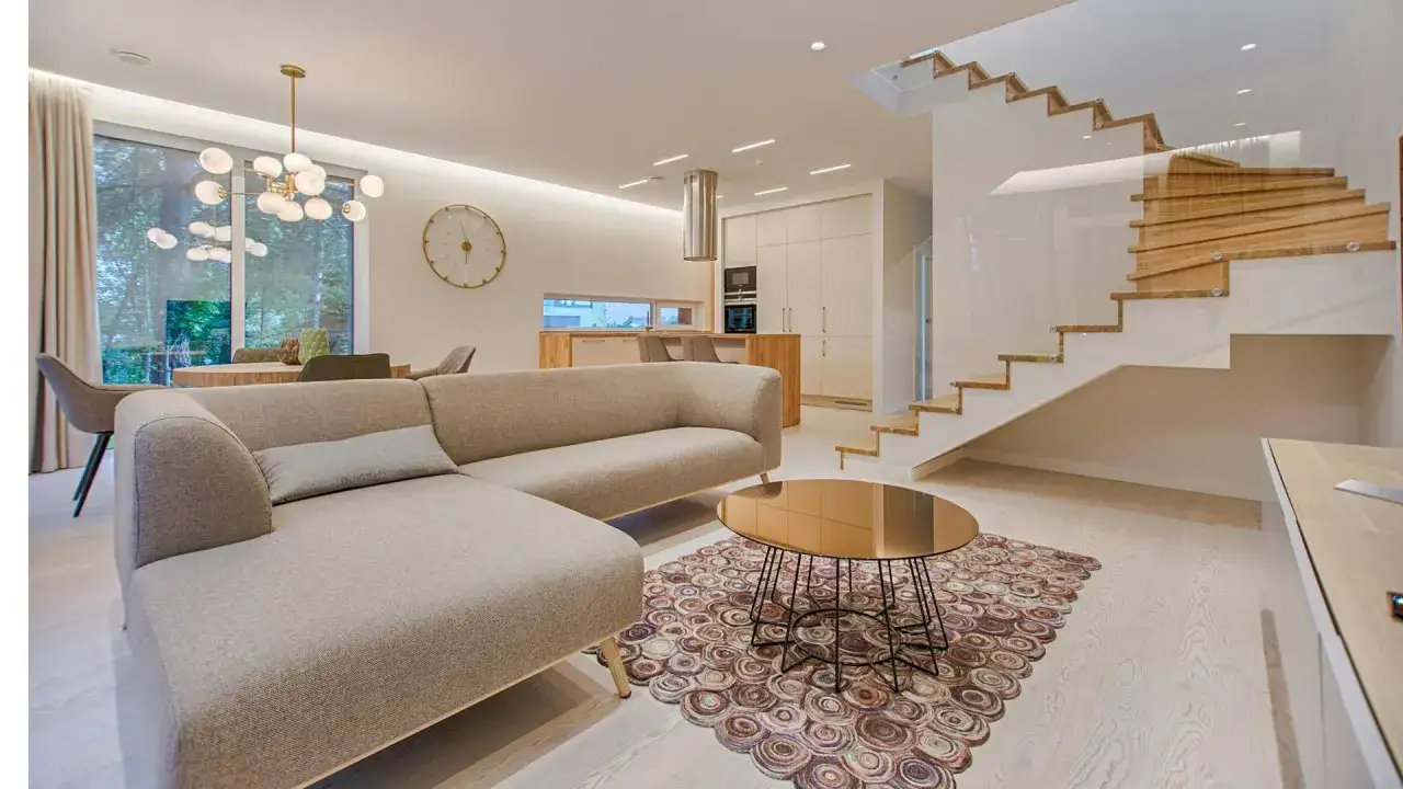 Un dise&ntilde;ador de interiores crea espacios modernos y funcionales, como este sal&oacute;n con sof&aacute; curvo, mesa de centro dorada y escaleras flotantes.