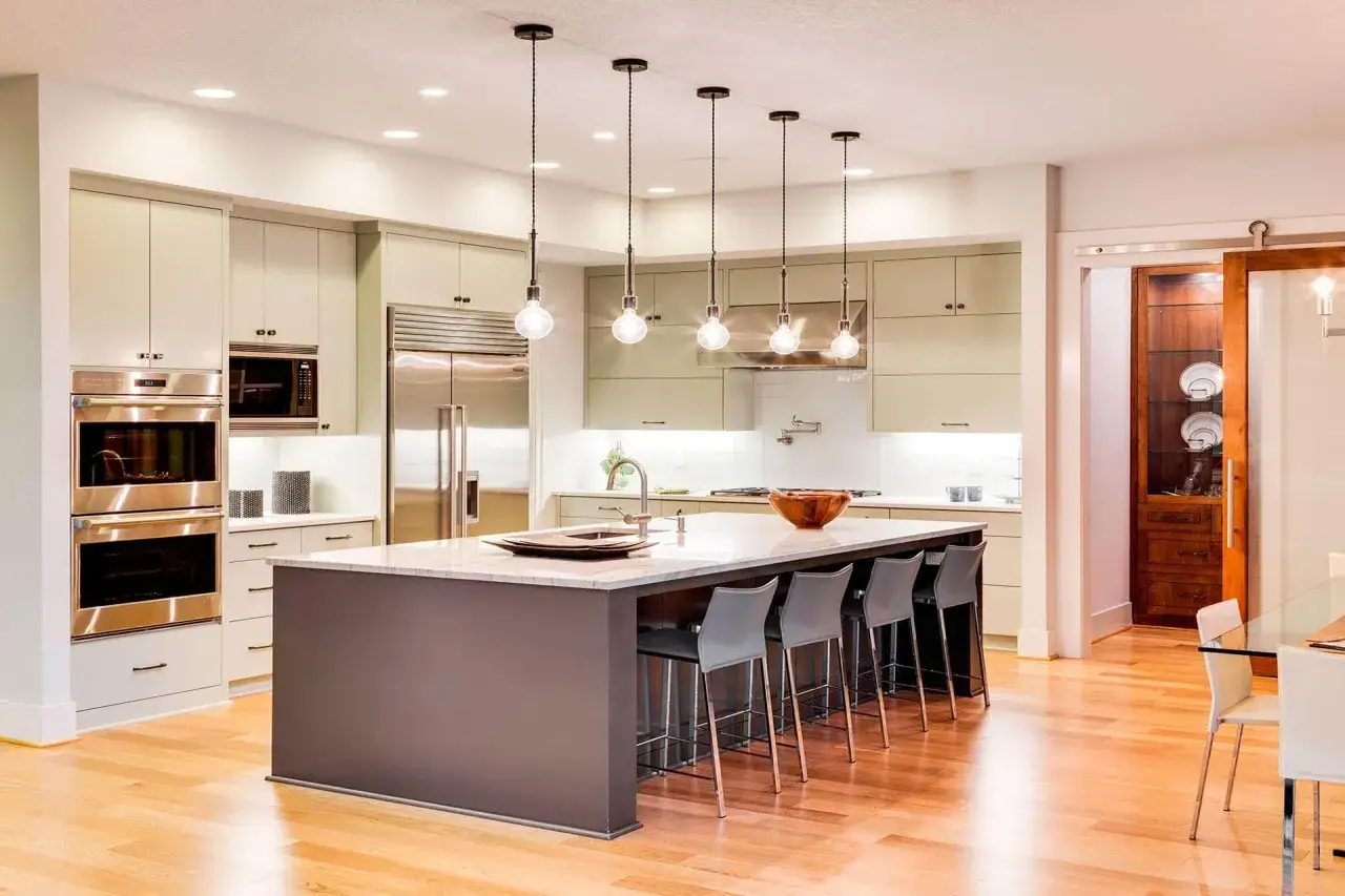Cocina moderna con isla central, electrodomésticos de acero inoxidable y varios tipos de luces: empotradas, colgantes y bajo gabinetes.
