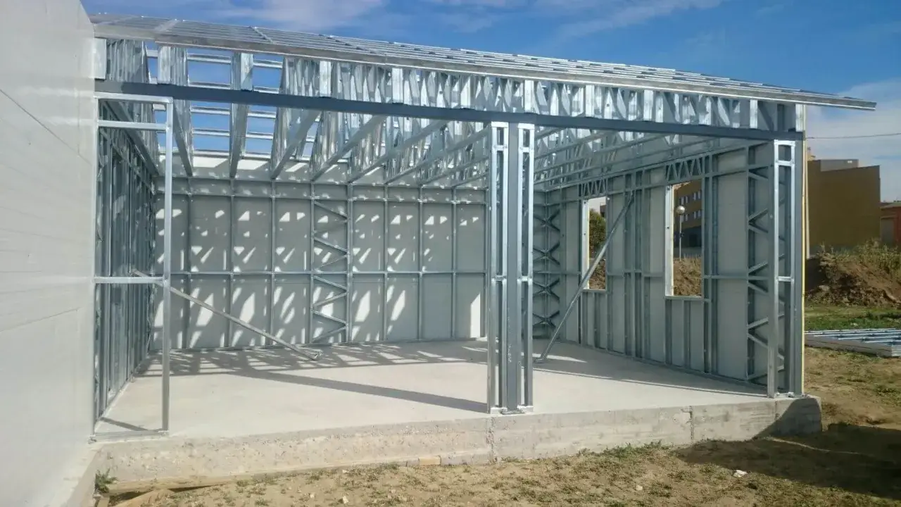 Estructura de steel frame en construcción, con paredes y techo metálicos expuestos, bajo un cielo azul.