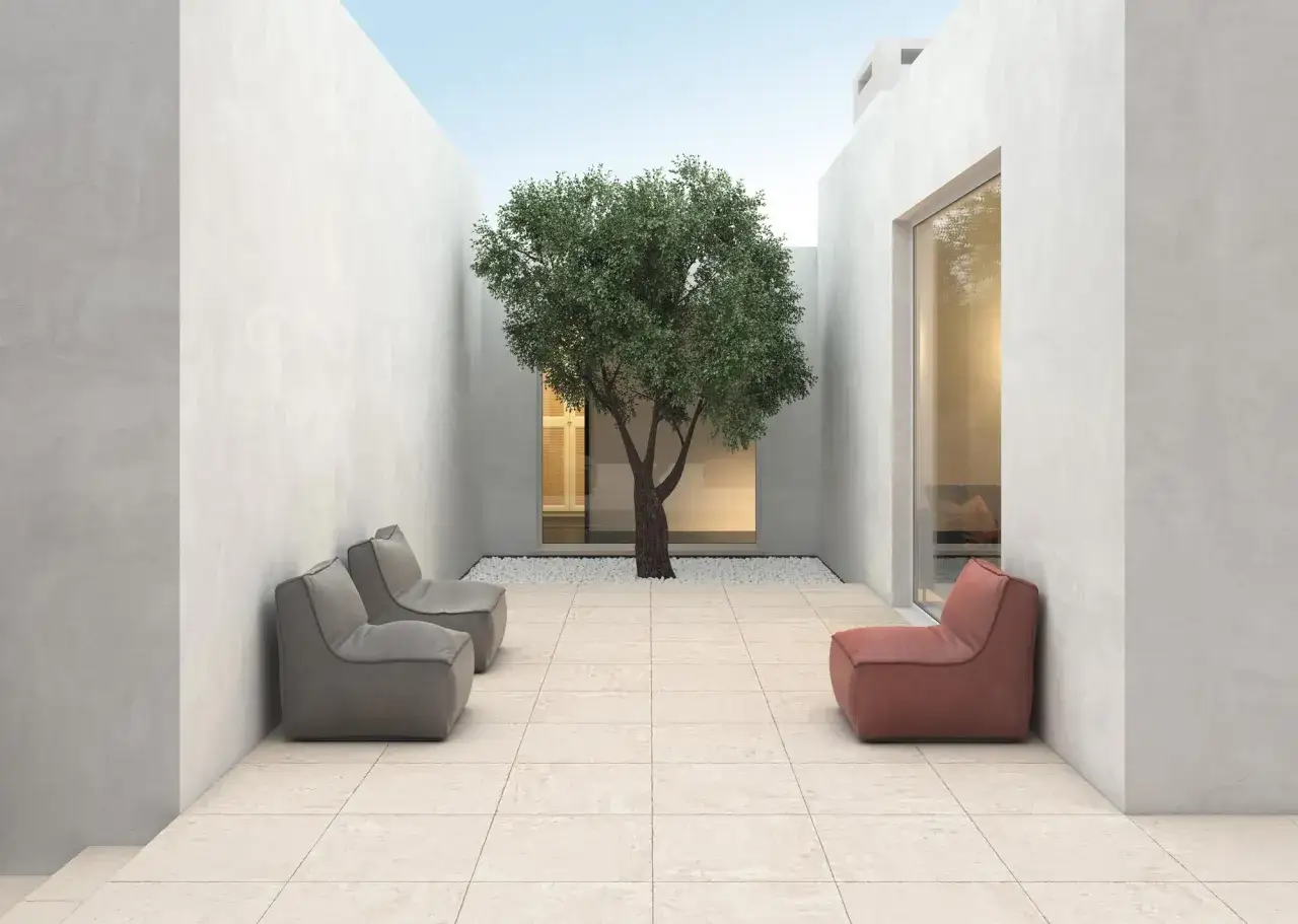 Patio moderno con suelo de porcel&aacute;nico que es de tonos claros, un &aacute;rbol frondoso en el centro y sillones de dise&ntilde;o.