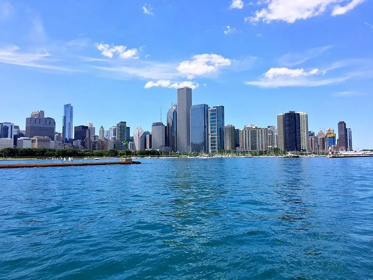 Impresionante vista de los chicago rascacielos reflej&aacute;ndose en el agua azul bajo un cielo despejado con nubes blancas.