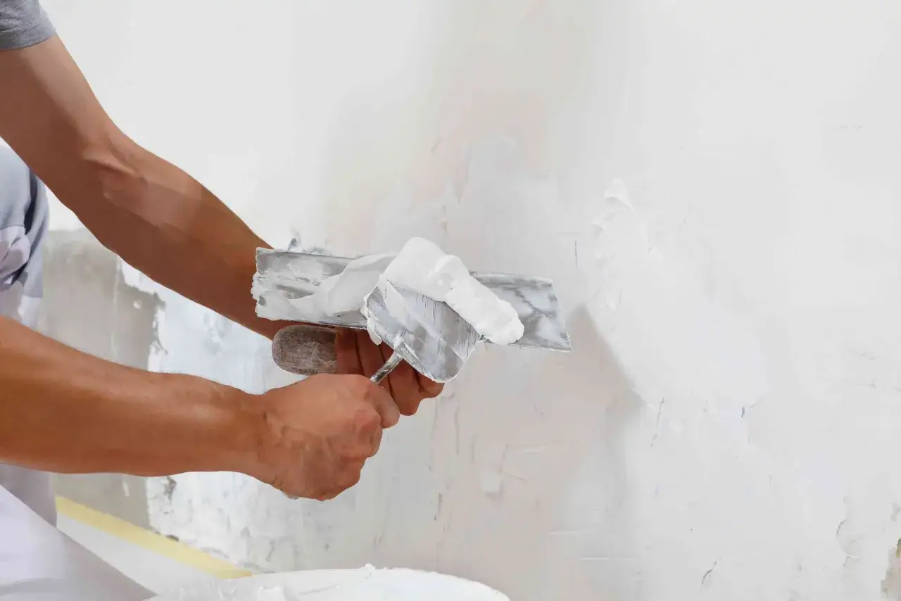 Man applying plaster to a wall, illustrating the diferencia entre enfoscado y guarnecido.
