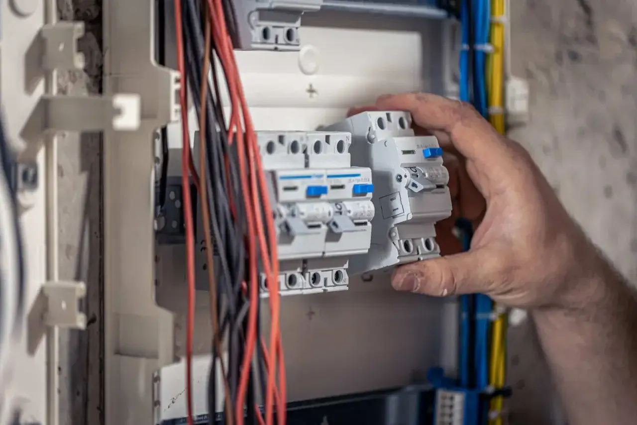 Mano instalando un interruptor autom&aacute;tico en un cuadro el&eacute;ctrico. Cableado rojo y negro visible. Instalaci&oacute;n el&eacute;ctrica vivienda.