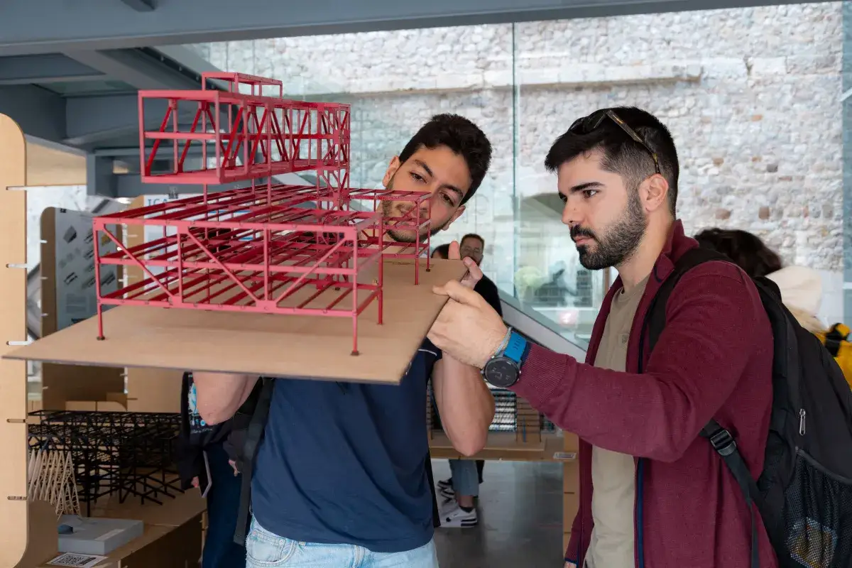 Estudiantes analizan un modelo arquitect&oacute;nico rojo, aprendiendo qu&eacute; hay que estudiar para ser arquitecto.