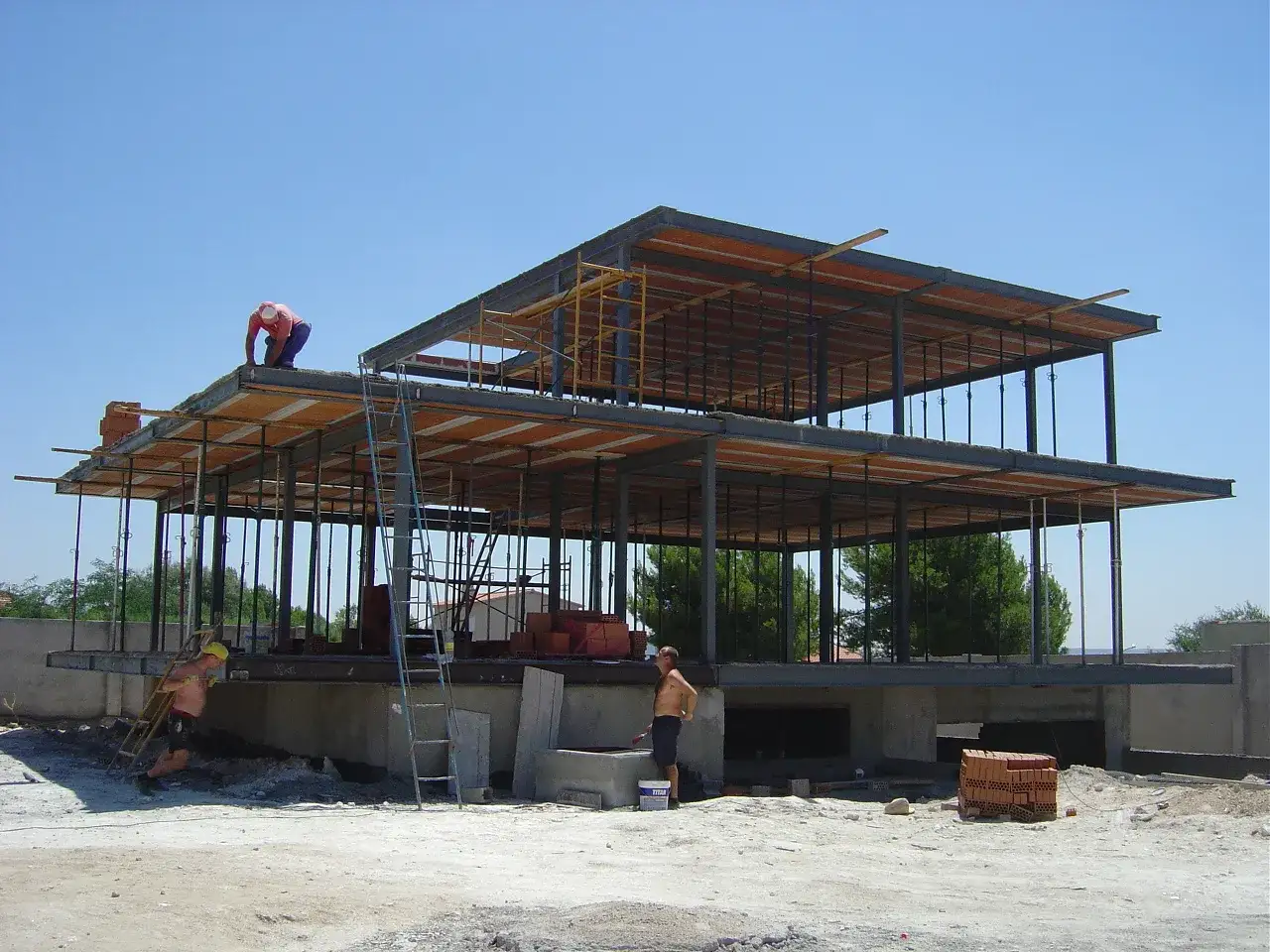 Obreros trabajan en la construcci&oacute;n de una casa de varios pisos. La estructura met&aacute;lica y las plataformas de madera est&aacute;n casi completas. Esto es un ejemplo de autopromoci&oacute;n, mostrando el progreso de la obra.