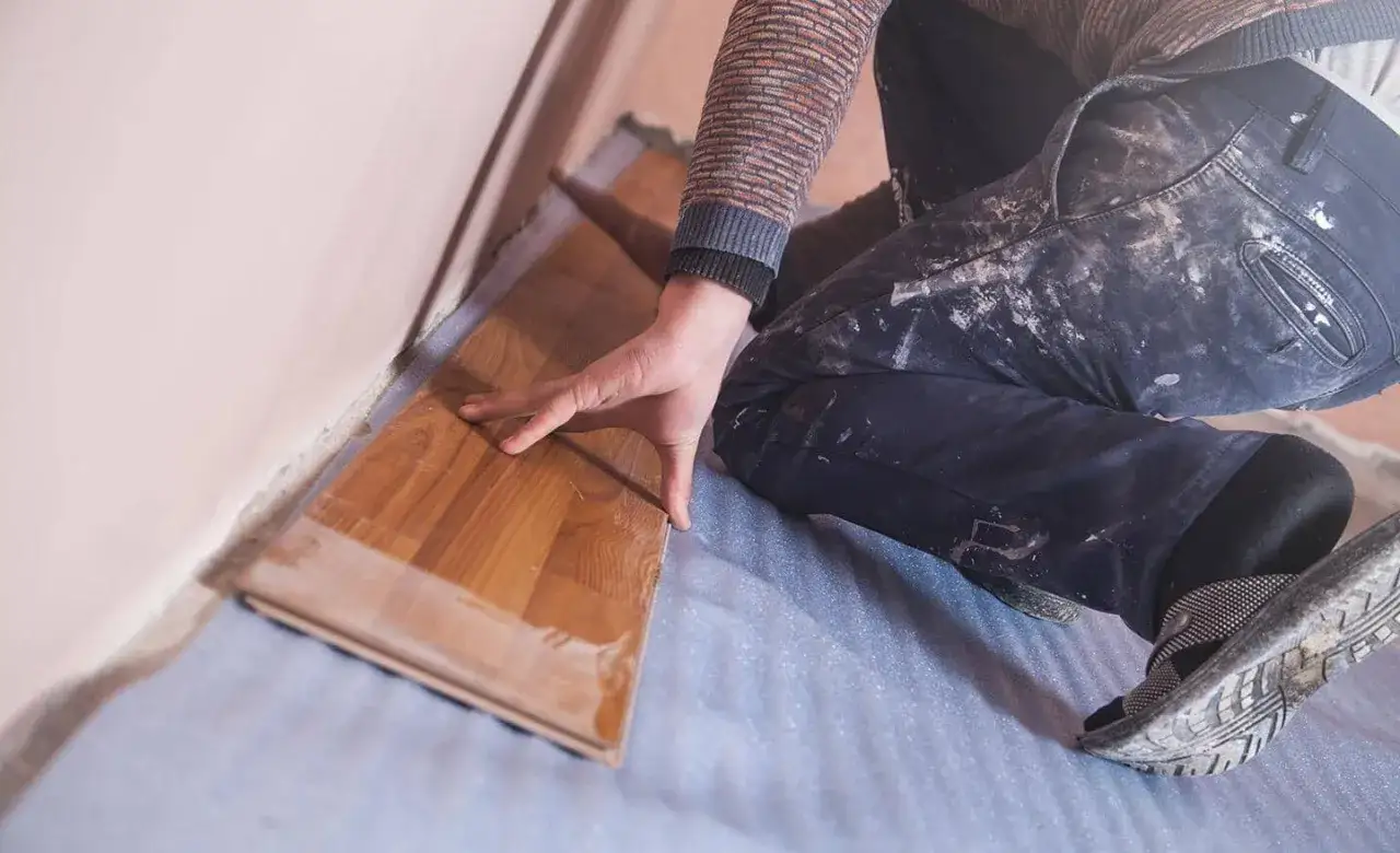 Man colocando suelo laminado de madera, con las manos sobre las tablas y la rodilla apoyada en el suelo.