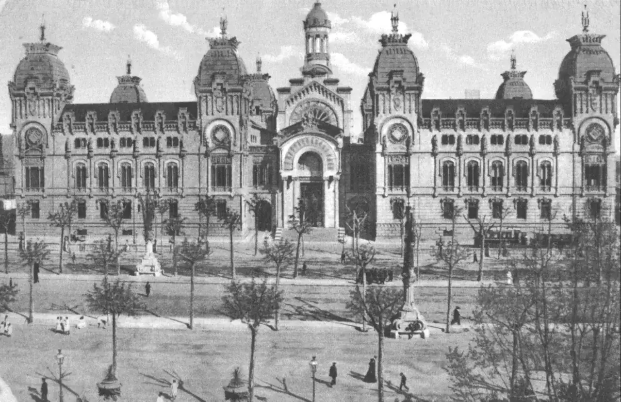 Edificio con c&uacute;pulas y arcos, reflejo del eclecticismo significado en la arquitectura. Personas pasean por la plaza arbolada.