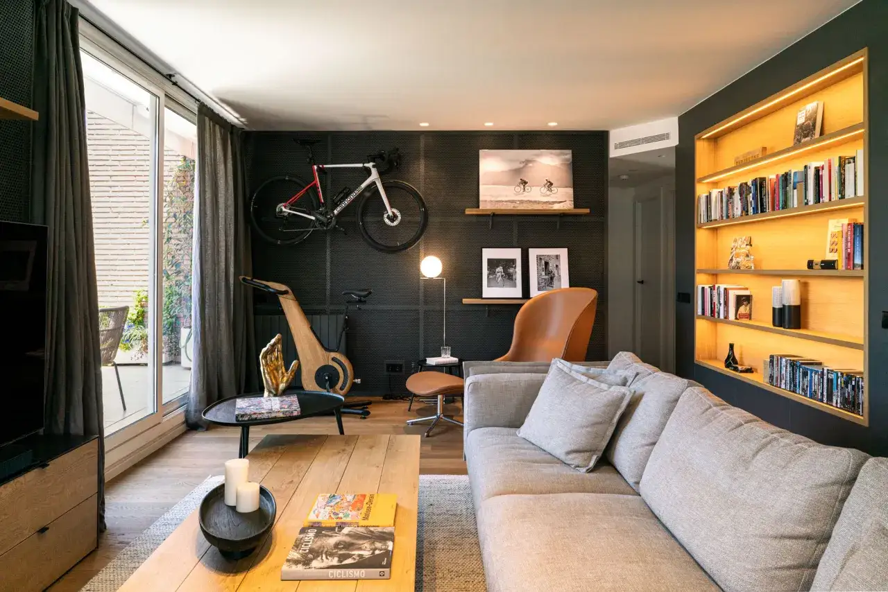 Sofá gris, bicicleta de carretera colgada, sillón de cuero y estanterías iluminadas, parte de unas modernas decoraciones de interiores.