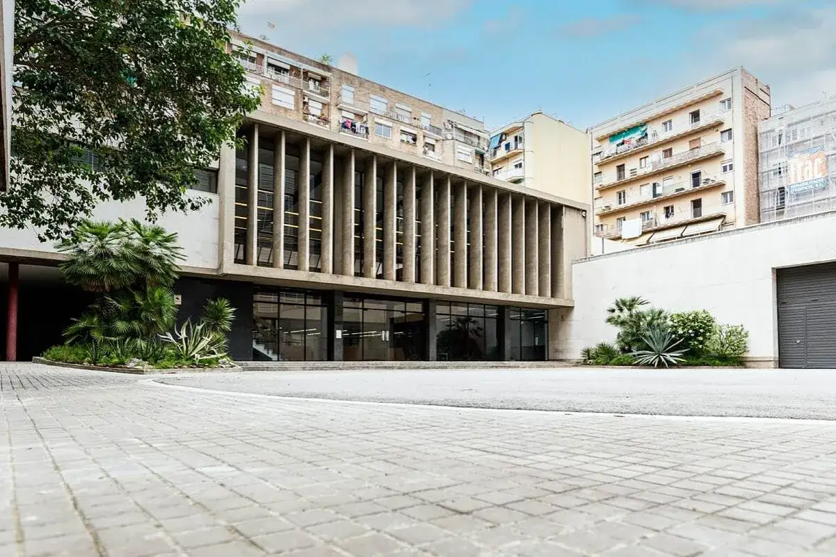 Edificio con fachada de concreto y ventanales amplios, un ejemplo de movimiento moderno arquitectura. Jard&iacute;n con palmeras y plantas des&eacute;rticas.