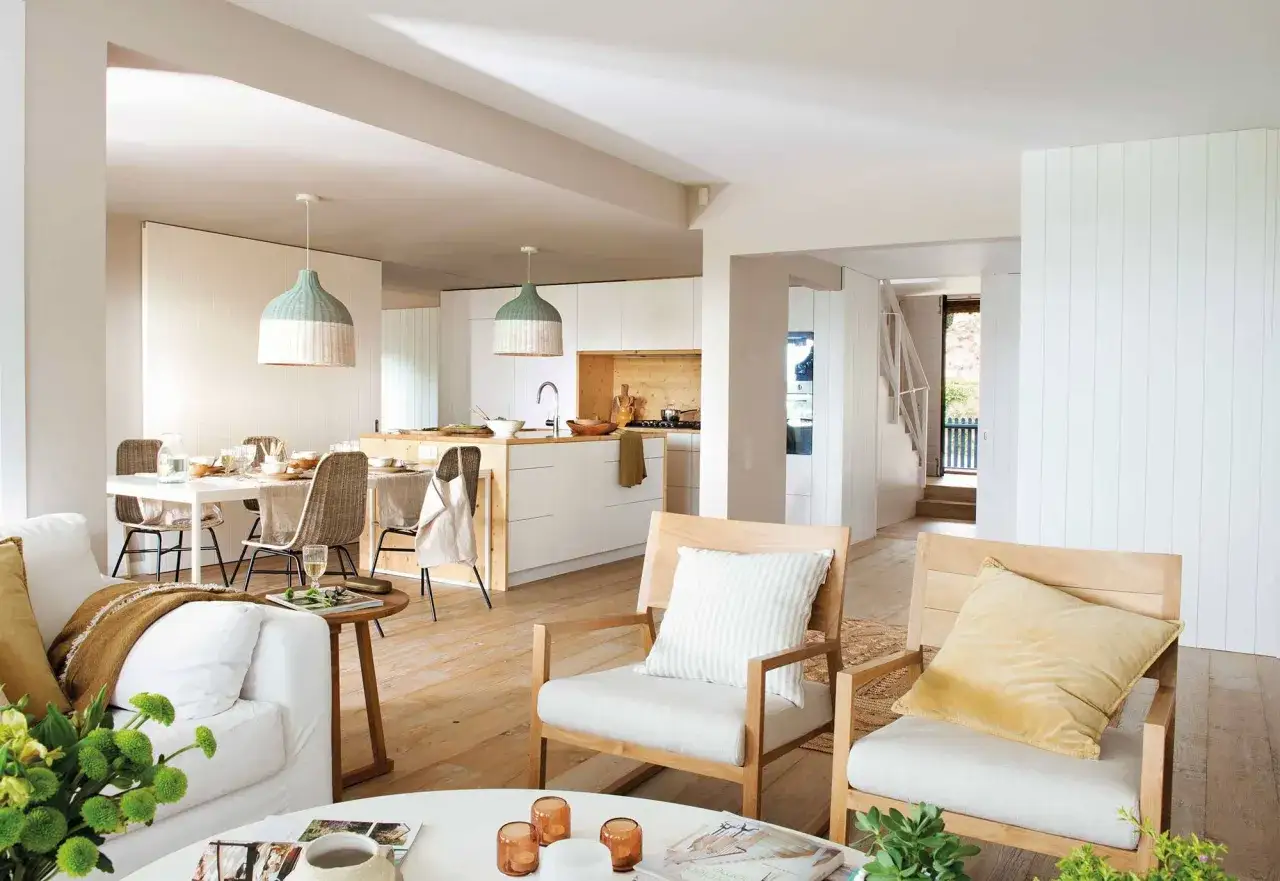 Un espacio diafano con sala, comedor y cocina integrados. Muebles de madera clara, textiles neutros y l&aacute;mparas colgantes de mimbre.