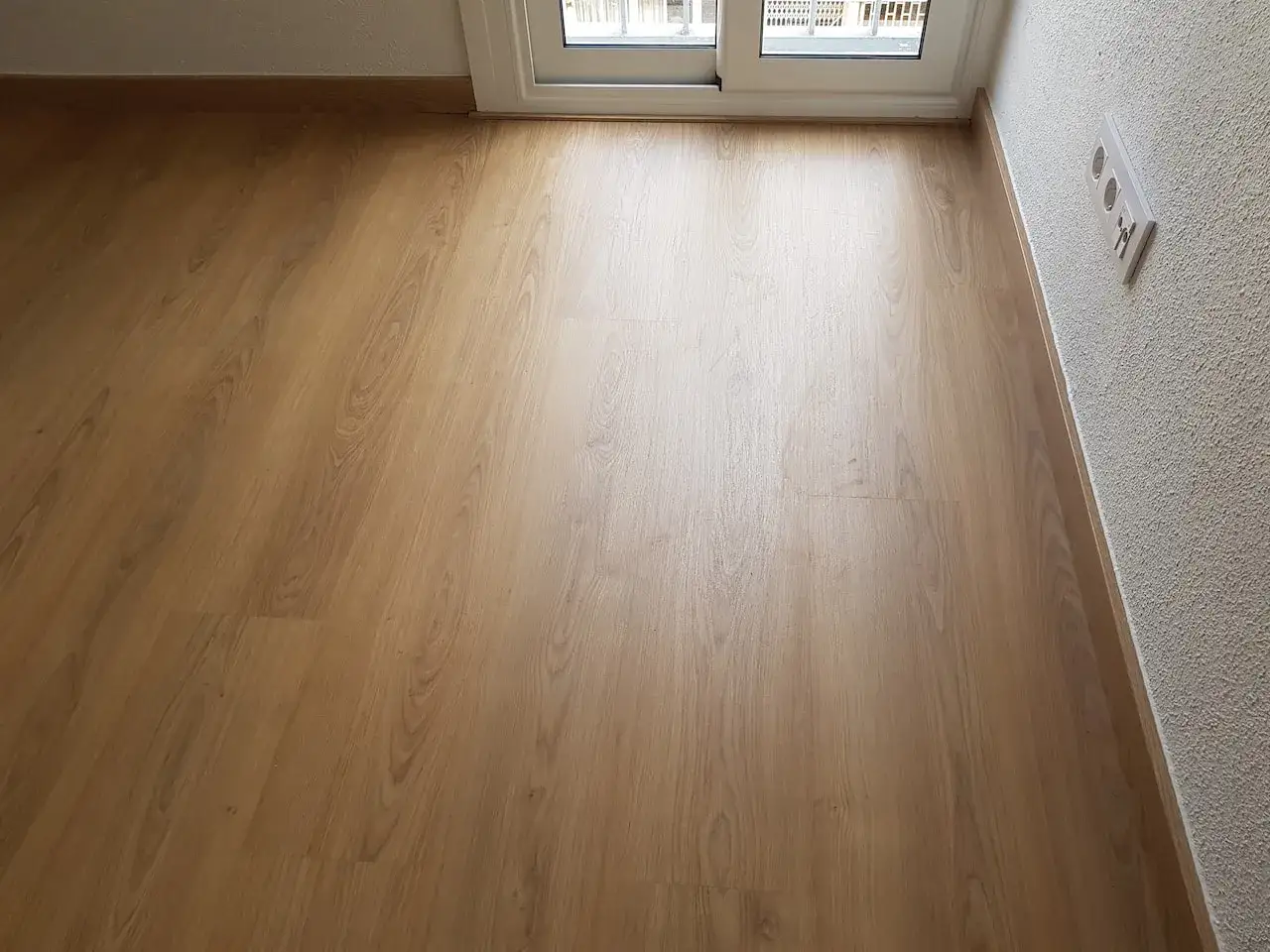 Suelo laminado de madera clara instalado en diagonal, mostrando la dirección en que colocar suelo laminado para un efecto visual óptimo.