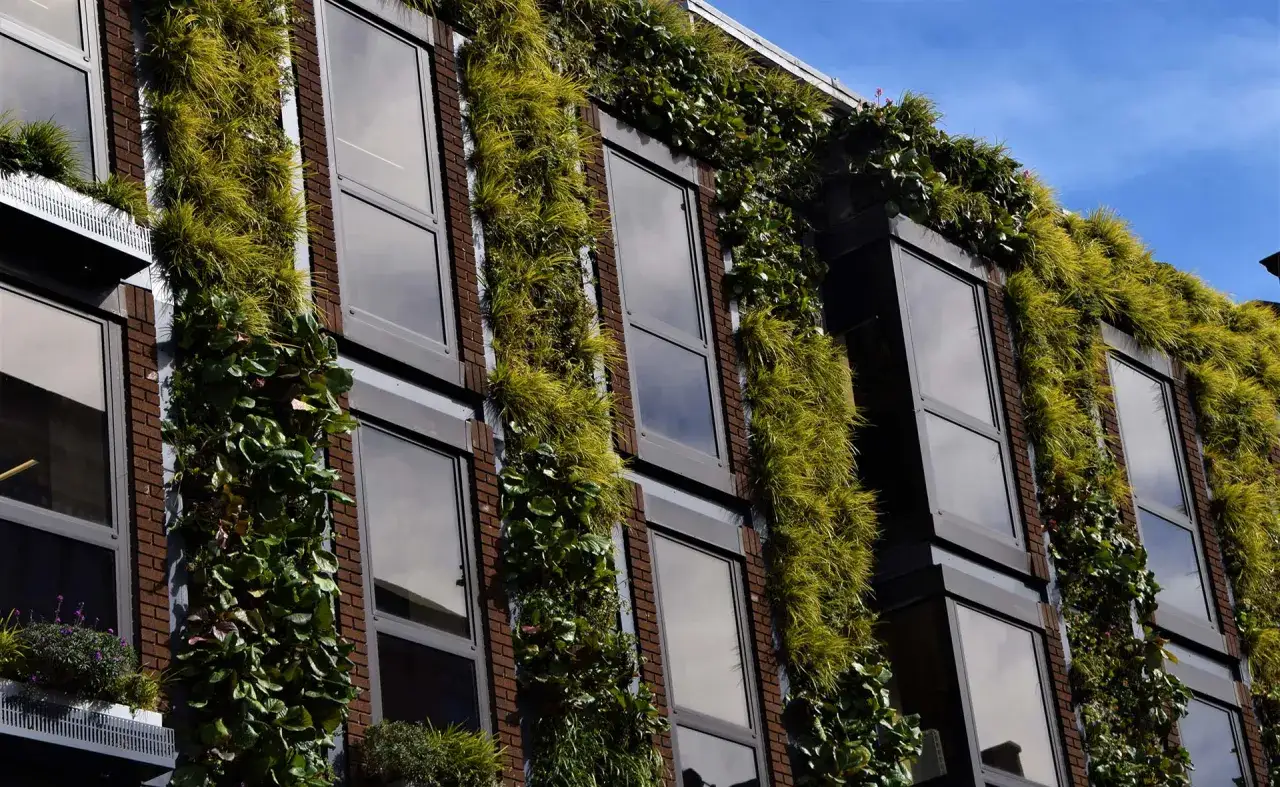 Edificio con fachadas verdes, un ejemplo de sostenibilidad en la construcci&oacute;n. Plantas cubren ladrillos y ventanas, integr&aacute;ndose con el entorno.
