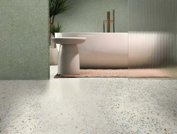 Baño moderno con bañera exenta y grifería dorada, sobre suelos de terrazo claros y paredes con el mismo acabado en tono verde.