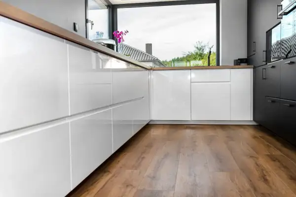 Cocina moderna con armarios blancos brillantes y encimeras de madera. El suelo vinílico SPC de madera aporta calidez y estilo.