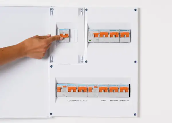 Panel de circuitos vivienda con interruptores naranjas. Una mano activa uno de los interruptores.