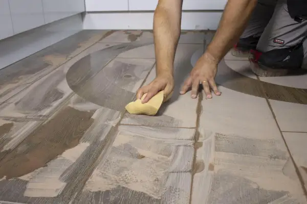 Man limpiando suelo porcelánico después de obra con una esponja, eliminando restos de cemento y polvo.