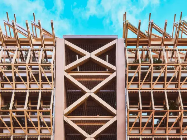 Estructura de madera con celosías y plantas, mostrando elementos de arquitectura moderna contra un cielo azul.