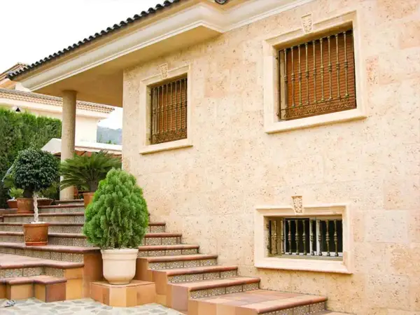 Fachada de casa con escaleras y plantas. Los distintos tipos de pared de piedra y detalles ornamentales resaltan la arquitectura.