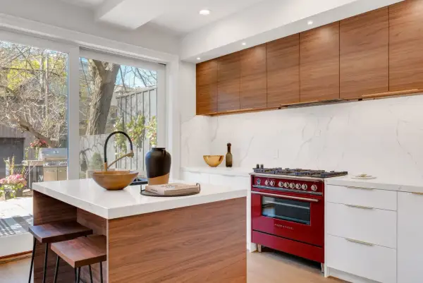 Cocina moderna con isla central, encimeras de cuarzo, gabinetes de madera y estufa roja. Un ejemplo de diseño de espacios interiores funcional y elegante.
