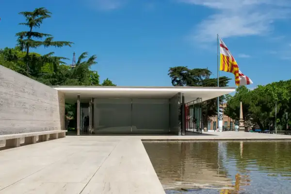 Pabellón de Mies van der Rohe, con su diseño minimalista, reflejos en el agua y una bandera catalana ondeando.
