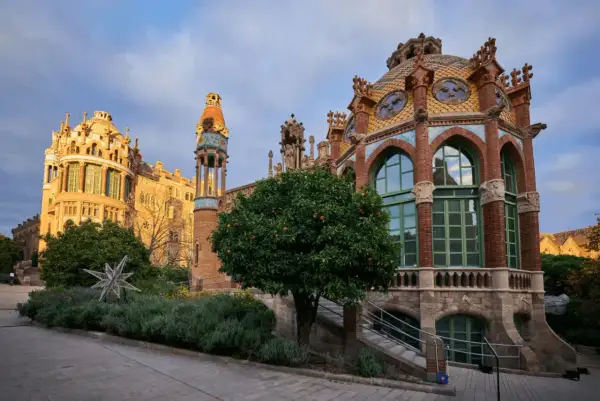 Edificios modernistas con cúpulas coloridas y arcos, rodeados de vegetación y un árbol frutal.