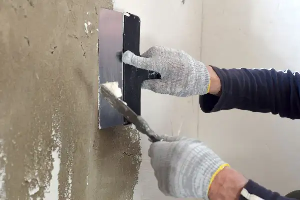 Manos enguantadas aplican yeso para sanear pared con llana.