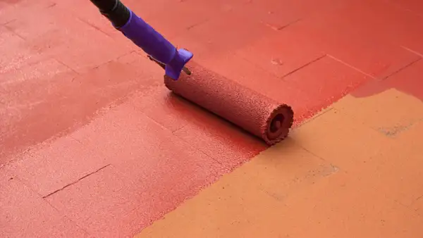 Rodillo morado pintando un suelo de baldosas con pintura roja, renovando el espacio.
