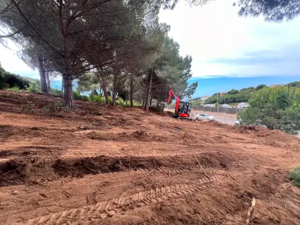 Excavadora roja trabaja en un solar urbano despejado, listo para construir.