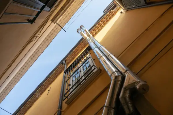 Dos tubos de acero inoxidable suben por la fachada amarilla de un edificio, parte del esquema bajantes edificio. Una ventana con rejas se ve debajo.