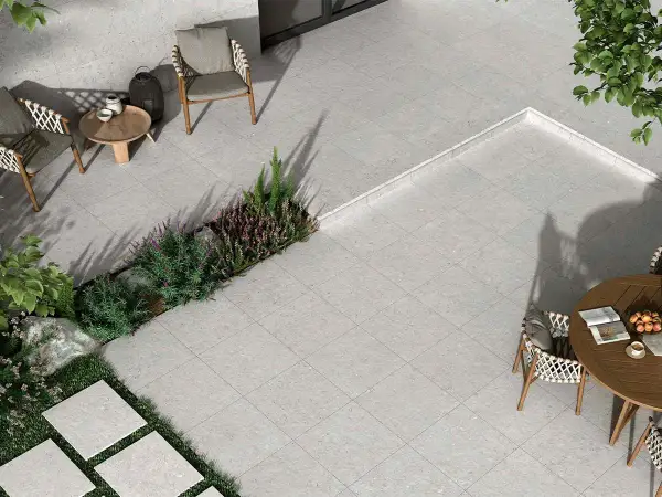 Terraza moderna con mobiliario de exterior y vegetación. El suelo está cubierto por un elegante **azulejo rectificado** de tonos grises, creando un espacio acogedor.