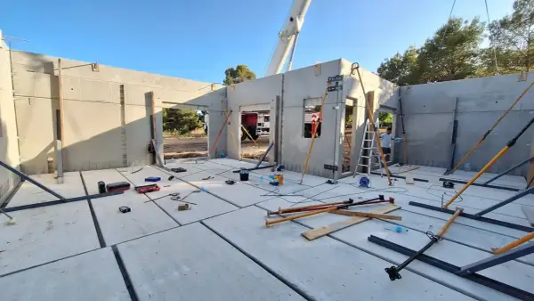 Construcción de casa con paneles prefabricados. Se ve el suelo de hormigón, paredes levantadas y herramientas. ¿Cuánto cuesta terminar una casa en obra?