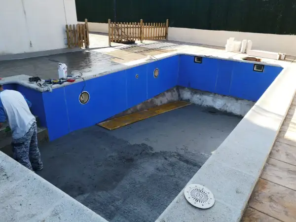 Piscina en construcción, paredes azules listas para recibir el gresite. Herramientas y materiales a un lado.