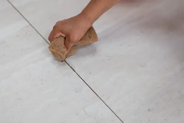 Mano aplicando lechada a las juntas de baldosas. Elige entre diversos colores de lechada para juntas para un acabado perfecto.