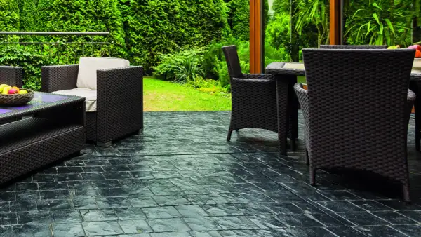 Terrazas con suelo de piedra oscura, muebles de mimbre y vegetación exuberante.